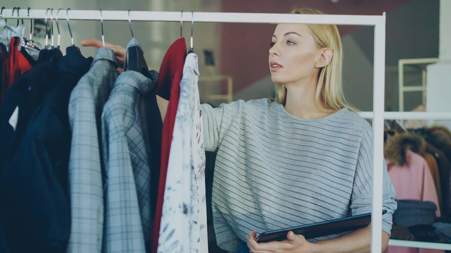 Woman with tablet selects clothes from a retail rack.